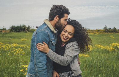 Brown haired man on the left in a denim jacket hugging a female with a grey shirt and curly hair