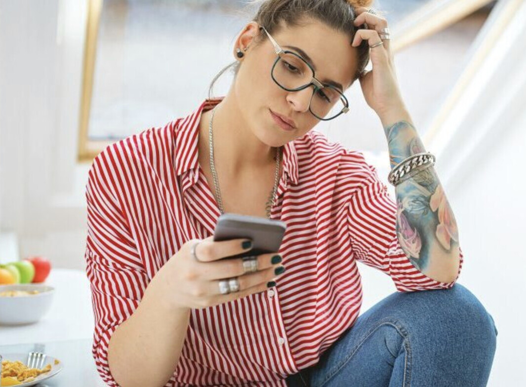 Femme presenting blonde female with an arm tattoo looking at her phone.