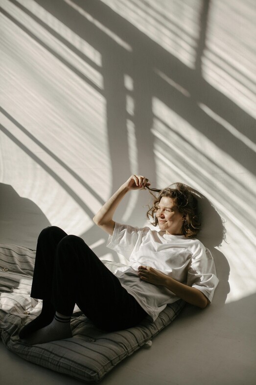 A girl laying down with a white shirt and sun pouring into the room. 